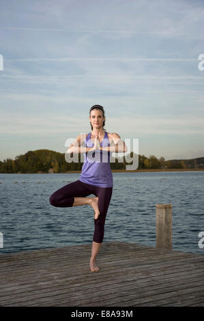 Woman practicing yoga on Jetty, Woerthsee, Bavière, Allemagne Banque D'Images