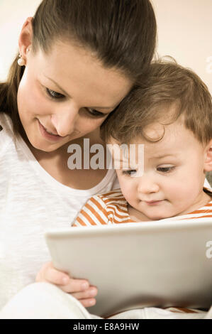 Mère et fils using digital tablet in living room, smiling Banque D'Images