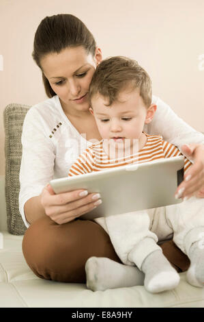 Mère et fils using digital tablet in living room, smiling Banque D'Images