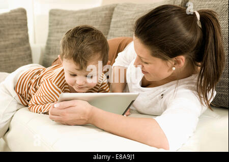 Mère et fils using digital tablet in living room, smiling Banque D'Images