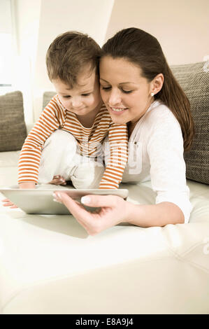 Mère et fils using digital tablet in living room, smiling Banque D'Images