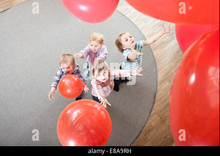Quatre enfants qui jouent avec des ballons rouges en maternelle, elevated view Banque D'Images