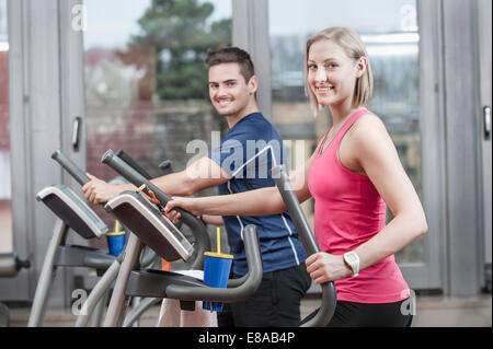 Jeune homme et femme sur elliptical trainer in gym Banque D'Images