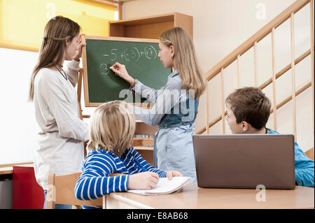 Assistant de garde d'aider les enfants de sexe féminin par faire leurs devoirs Banque D'Images