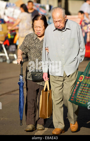 Vieux couple chinois s'aident mutuellement à traverser la rue sur Chun Yeung Street, North Point, Hong Kong. Banque D'Images