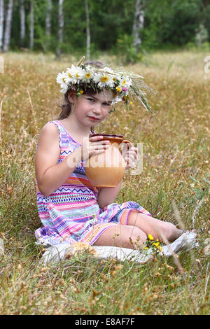 Petite fille assise sur l'herbe avec verseuse en mains. Ses lèvres des traînées dans le lait Banque D'Images