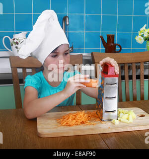 Petite fille frotte sur la carotte dans la cuisine râpe Banque D'Images