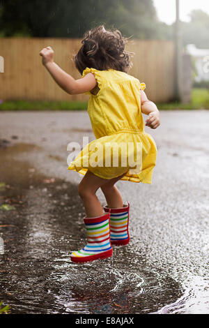 Porter des bottes de caoutchouc fille sautant dans la pluie flaque Banque D'Images