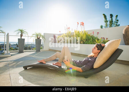 Mid adult woman lying on chaise longue dans le jardin sur le toit, La Jolla, Californie, USA Banque D'Images