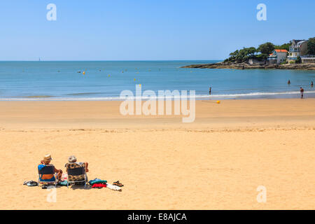 Couple d'âge moyen assis dans des chaises pliantes sur plage tranquille. Banque D'Images