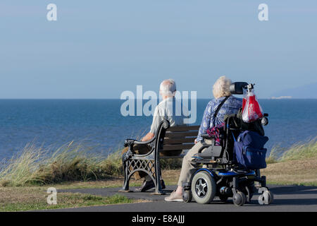 Homme assis sur un banc avec son épouse en fauteuil roulant sur un sentier côtier à Blackpool, lancashire, uk Banque D'Images