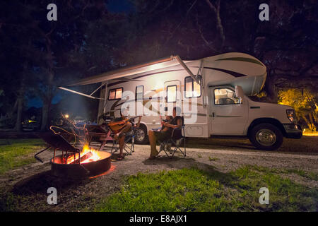 Couple et sa petite fille assise devant un feu de camp la nuit Banque D'Images