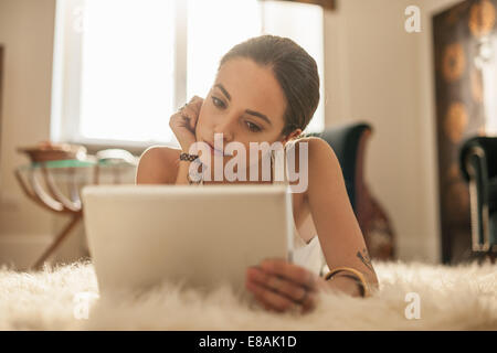 Young woman lying on salon tapis looking at digital tablet Banque D'Images