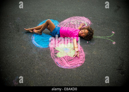 Young Girl lying on floor entre à la craie les ailes de papillon Banque D'Images