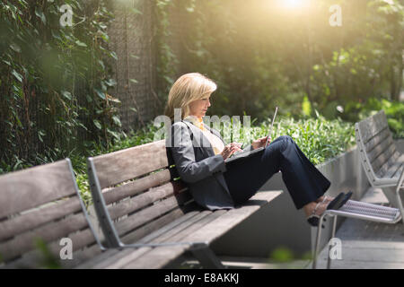 Mature businesswoman sitting on bench using laptop Banque D'Images