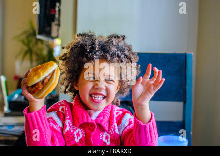 Cute girl rire et holding up hamburger en cuisine Banque D'Images