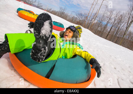 Garçon riant tout en bas du toboggan snowy hill Banque D'Images