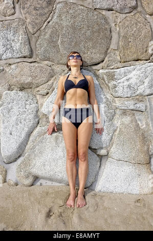 Une femme dans la mi-quarantaine allongée de soleil contre un mur, Cornwall, UK Banque D'Images