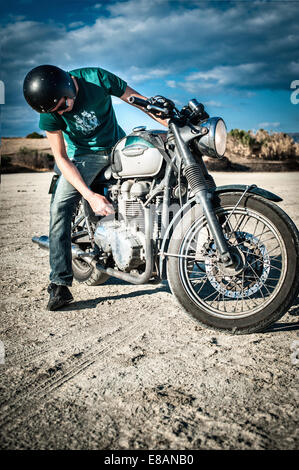 Mid adult man checking sur moto plaine aride, Cagliari, Sardaigne, Italie Banque D'Images