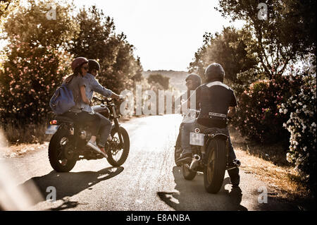 Vue arrière de quatre amis à motocyclette chatting on rural road, Cagliari, Sardaigne, Italie Banque D'Images