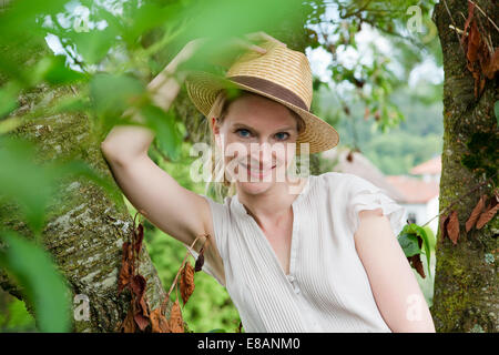 Portrait of mid adult woman in straw hat à côté arbre de jardin Banque D'Images