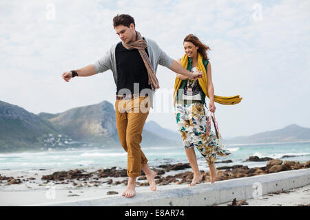 Jeune couple en train de marcher le long de bloc de ciment sur Beach, Cape Town, Western Cape, Afrique du Sud Banque D'Images