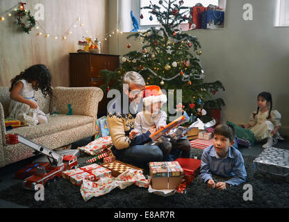 Père et quatre enfants d'ouvrir les cadeaux de Noël dans la salle de séjour Banque D'Images