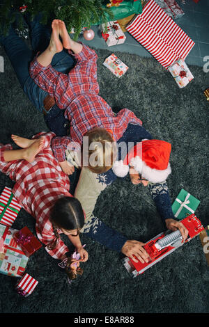 Père couché sur salon-de-chaussée de l'ouverture des cadeaux de Noël avec ma fille et fils Banque D'Images
