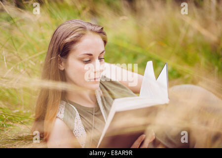 Jeune femme assise dans l'herbe haute reading book Banque D'Images