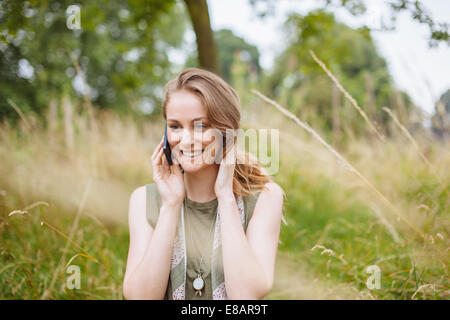 Young woman chatting on smartphone in field Banque D'Images