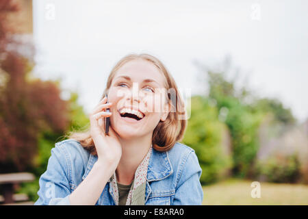 Jeune femme en riant tout en bavardant sur smartphone in park Banque D'Images