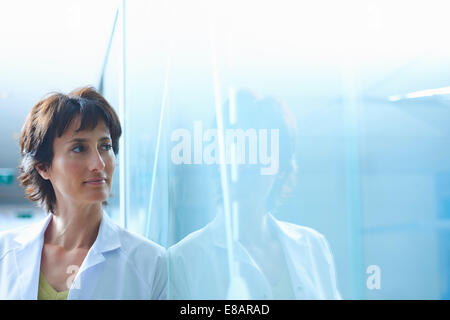 Confiant mature businesswoman leaning against glass wall in office Banque D'Images