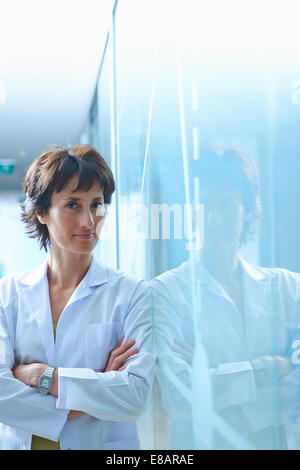 Portrait of mature businesswoman leaning against glass wall in office Banque D'Images