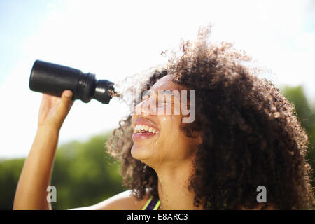 Jeune femme versant de l'eau sur le visage en park Banque D'Images