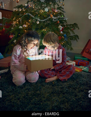 Soeur et frère bouche ouverte sur lumineux unwrapping christmas gift box Banque D'Images