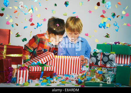 Deux frères bouche ouverte sur lumineux unwrapping christmas gift box with exploding confetti Banque D'Images