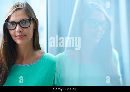 Portrait of mid adult businesswoman leaning against glass wall in office Banque D'Images