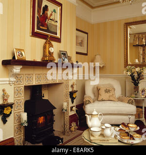 Service à thé sur la table en face de cheminée avec des tuiles décoratives et poêle à bois dans la salle de séjour avec papier peint à rayures Banque D'Images