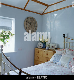 Vieille horloge ronde en bois sur le mur en bleu pâle cottage chambre avec commode pin à côté de lit en laiton antique Banque D'Images