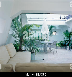 Parapluie blanc au-dessus de table à manger et chaises en métal dans des voitures-conversion loft avec de grandes plantes d'intérieur et toit en verre Banque D'Images