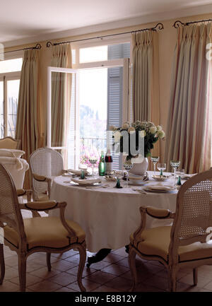 Canne ancienne-chaises à table avec un tissu blanc fixé pour le déjeuner en face de windows en français à manger côtières Banque D'Images