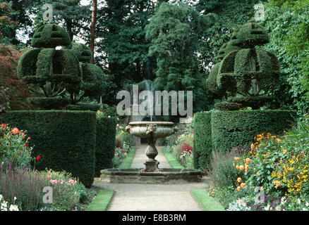 Topiaire clippé couronnes sur chaque côté de la fontaine en pierre au grand pays jardin avec fleurs colorées en été les frontières Banque D'Images