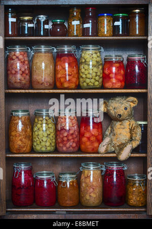 Un ours en peluche aux yeux élimés sur une planche en bois avec des bouteilles stockées des fruits, des confitures et des conserves Banque D'Images