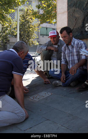 Les hommes de jouer à un jeu de 'titzmitz' dans l'ombre de la statue de l'Inconnu, partisan dans le centre de Tirana, Albanie Banque D'Images