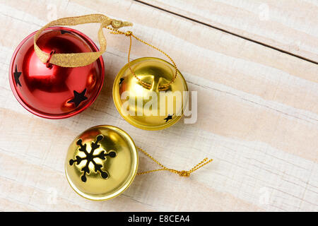 High angle view of trois Jingle bells sur une table en bois blanc. Deux cloches d'or et un rouge en format horizontal avec l'exemplaire de l'espace. Banque D'Images