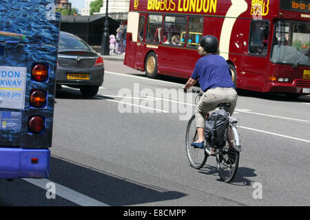 Un cycliste et location de dépasser un autobus stationnaire à Londres. Un bus de tournée se déplace dans la direction opposée. Banque D'Images