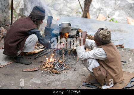 Deux vieux amis Sadhus assis sur croupes par leur feu (dhuni) plateau de cuisson (chai) au-dessus des rives de la rivière Gange Rishikesh Banque D'Images