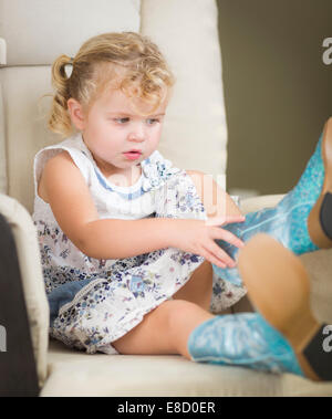 Blond aux yeux bleu adorable petite fille mettant sur bottes de cow-boy. Banque D'Images