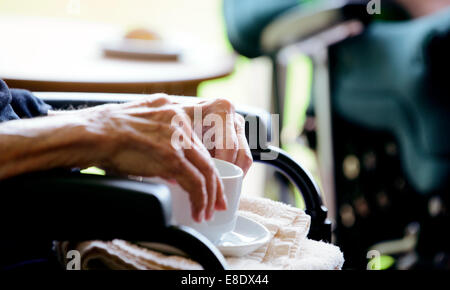 Une personne âgée dans un fauteuil roulant est remis une tasse de thé par du personnel infirmier. Banque D'Images