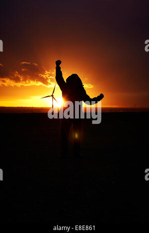 Silhouette d'un homme tenant dans ses bras jubilation derrière un coucher de soleil couleur orange foncé. long shot. Banque D'Images